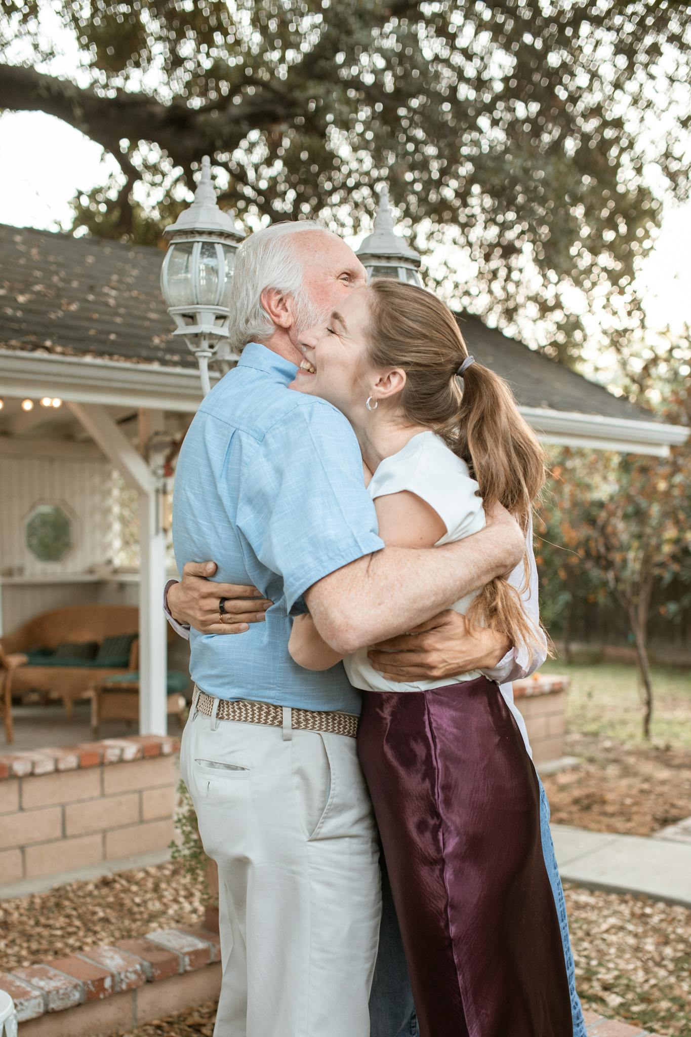 A touching moment between an elderly father and his adult daughter sharing an embrace in a garden.