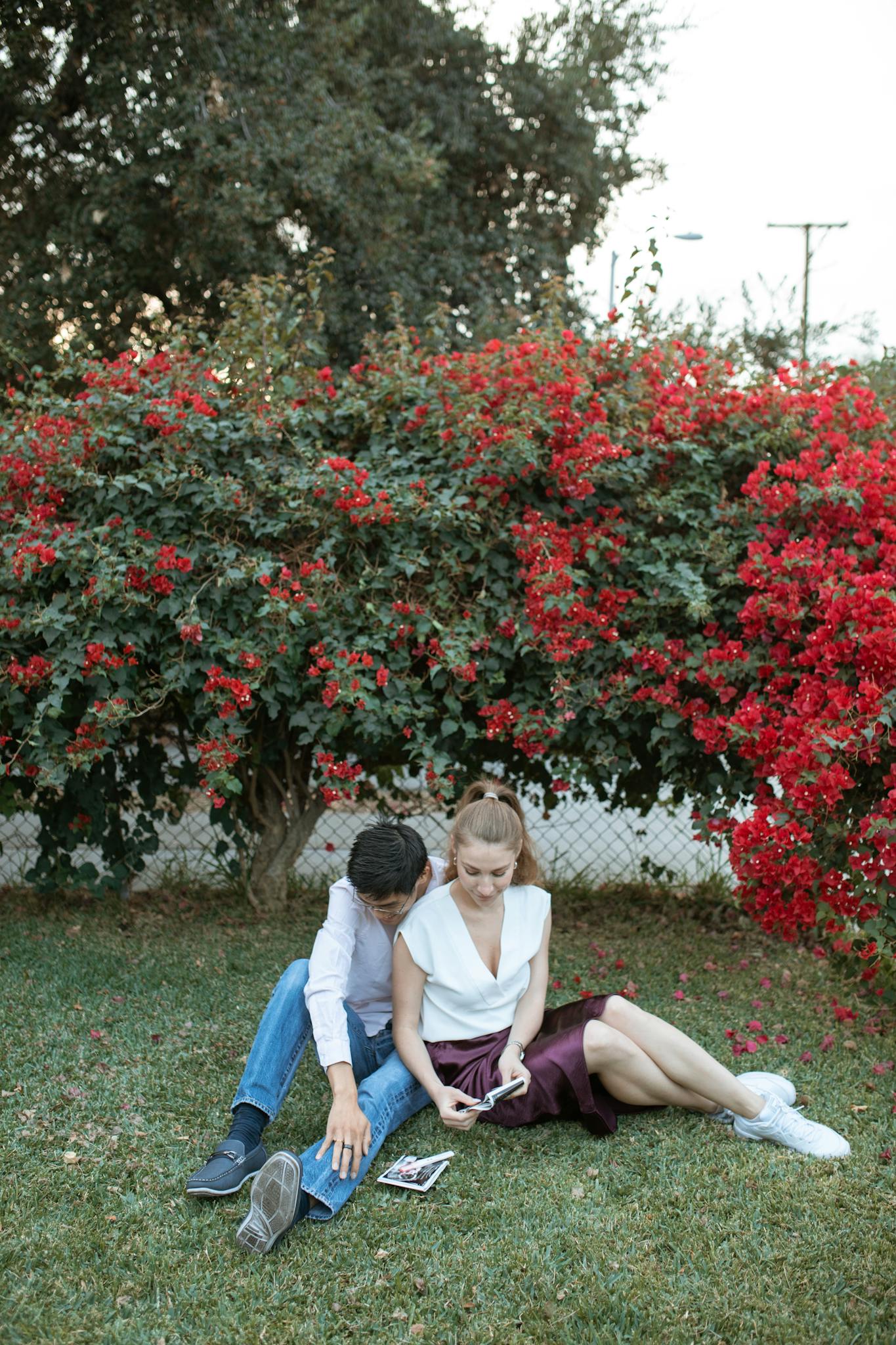 Couple sitting on grass, surrounded by vibrant flowers, sharing a tender moment.