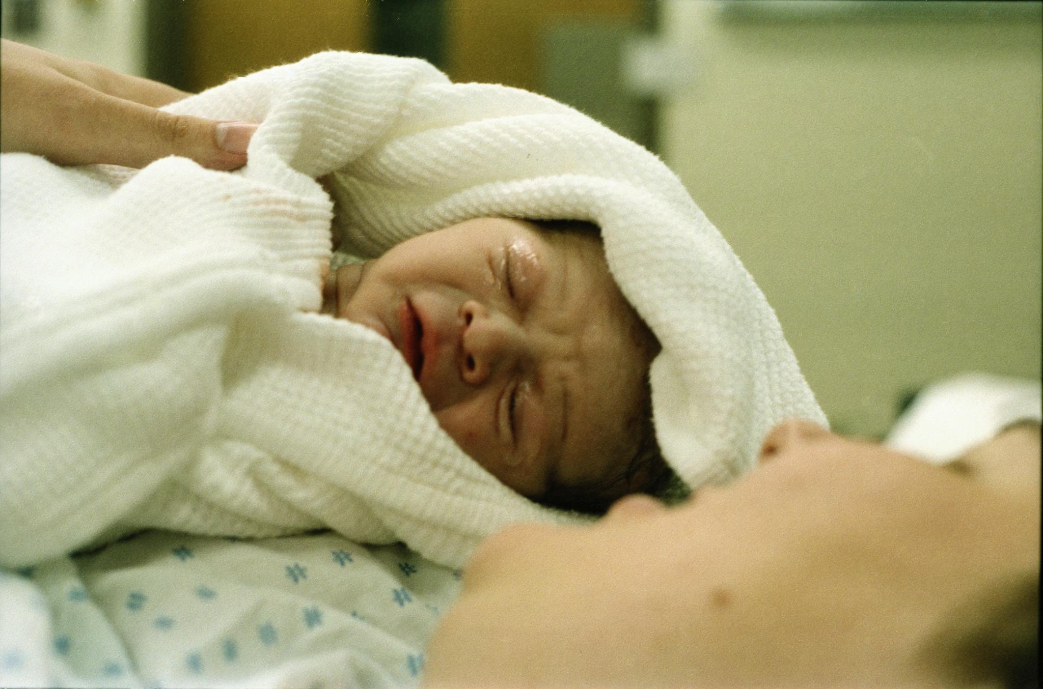 Tender image of a newborn baby wrapped in a white blanket at the hospital.